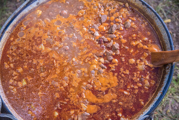 Mixing and cooking pork and beef goulash in big caldron made on fire
