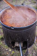 Mixing and cooking pork and beef goulash in big caldron made on fire