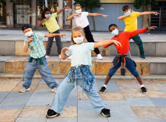 Preteen boys and girls breakdancers in medical masks dancing on city street in summer. Concept of precautions during coronavirus pandemic.