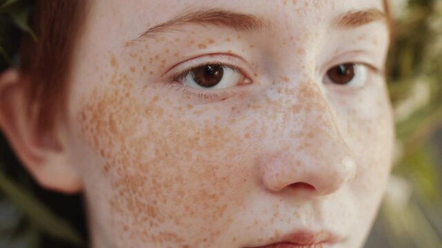 Close up selective focus shot face of young redhead woman with lots of freckles posing for camera in flower wreath