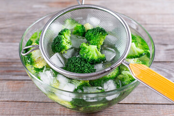 Blanched broccoli cabbage florets in a sieve in icy water on wooden table