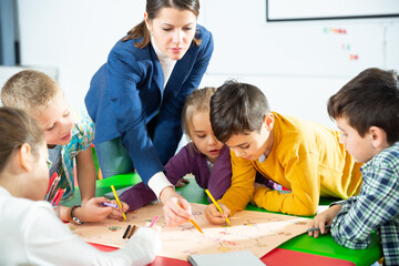 Happy kids and female teacher playing together educational board game in classroom at elementary school