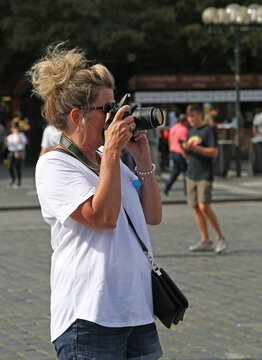 Adult blonde woman in sunglasses takes pictures with a DSLR camera.