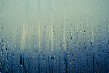 Water drops on the fogged glass with a brightness gradient of a muted blue background