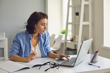 Woman sitting with laptop and notebook, watching online lesson or videocall and making notes