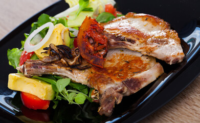 Tasty frying pork loin at plate with salad from avocado, tomatoes and corn salad