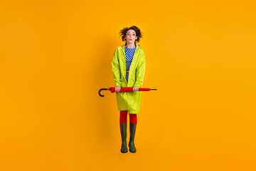 Full length photo portrait of shocked girl jumping up holding closed umbrella in two hands isolated on bright yellow colored background
