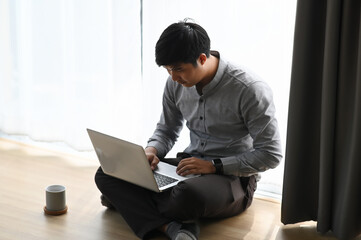 Fototapeta premium A youn businessman working on his project with laptop while sitting on floor at his room.