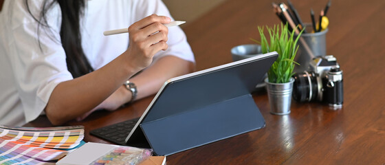 Cropped shot of attractive female designer using tablet for work while sitting in office.
