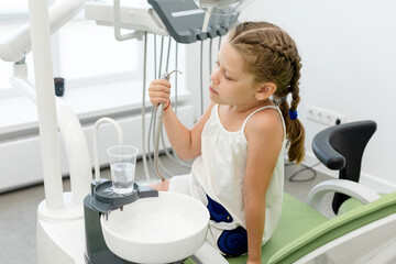 Little girl playing at the dentist. caucasian girl pours water into a plastic cup from dental equipment. Visiting dentist with children.