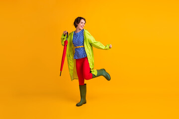 Full length photo portrait of funny woman standing on one leg with umbrella isolated on bright yellow colored background