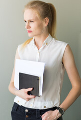 Confident pensive business woman standing holding a notebook and documents.