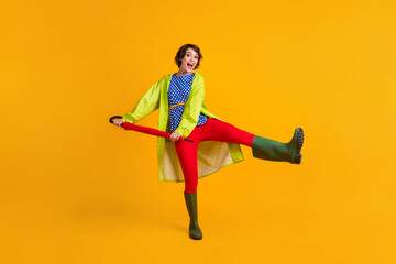 Full length photo portrait of girl kicking standing on one leg holding umbrella with two hands isolated on vivid yellow colored background