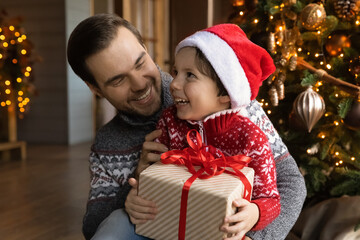 Obraz na płótnie Canvas Overjoyed loving young Caucasian father and small son celebrate New Year at home together. Caring dad greeting congratulating excited little boy child present Christmas gift. Winter holiday concept.