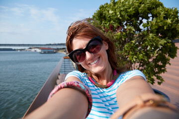 Young woman taking selfie outdoors near the river in city environment.