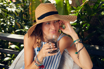 Young caucasian woman sitting on a patio and drinking coffee / tea in summertime season.