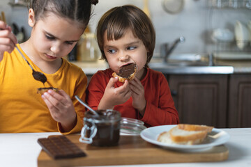 Sister and brother alone in the kitchen have breakfast on their own chocolate paste, smeared on the...