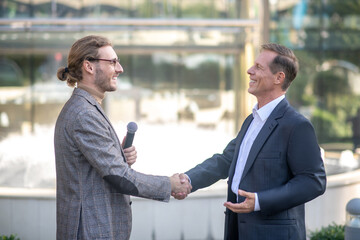Male interviewee and fair-haired male journalist shaking hands outside