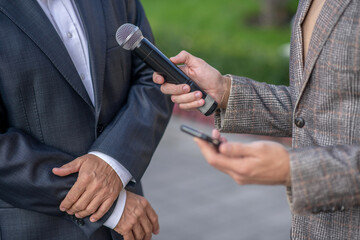 Close-up of male hands holding microphone and smartphone, recording interview