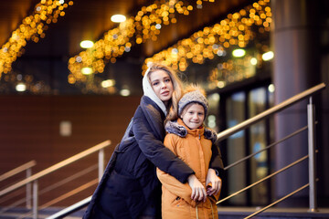 Two sisters friend outdoor in autumn winter in jackets and hats, older sister spends time together, walking around the winter city
