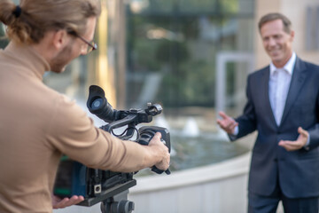 Fair-haired operator filming mature male report outside