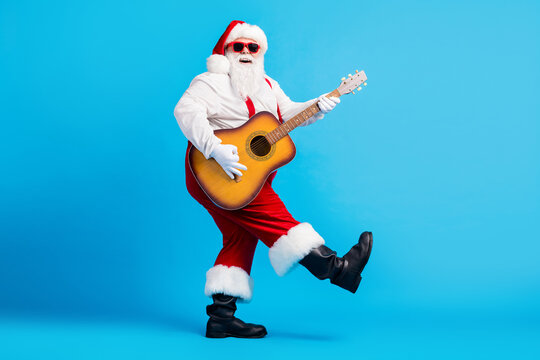 Full size photo of crazy cool santa claus with big belly beard play guitar x-mas christmas performance wear sunglass suspenders overalls isolated over blue color background