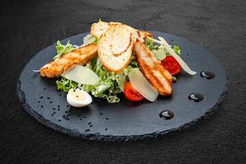 Caesar salad with chicken on a dark stone board.