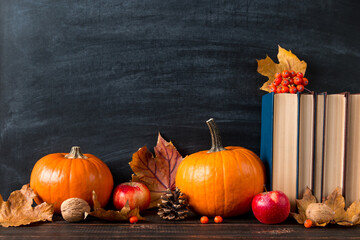 Pumpkin, fallen yellow leaves, books and apples on the table, chalkboard. Template for design. The concept of autumn mood, halloween and Thanksgiving.