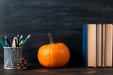 Teacher's table, books, pencils, pens, fallen leaves, glasses and an apple, on chalkboard background. Template concept of autumn mood. Copy space.