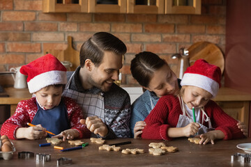 Happy young Caucasian parents with two small kids have fun decorate Christmas biscuits in kitchen together. Smiling family with little children baking cookies for New Year winter holidays celebration.