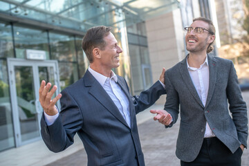 Two smiling male colleagues having friendly conversation outside