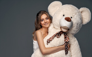 Beautiful cheerful young girl with cute big bear isolated on gray background