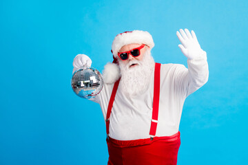Fototapeta na wymiar Photo of cool funky overweight santa claus dance x-mas christmas newyear party hold disco ball wear suspenders overalls sunglass isolated over blue color background