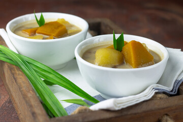 Kolak Ubi labu Kuning, Indonesian popular dessert made from pumpkin, sweet potato, coconut milk, and palm sugar. Served on ceramic bowl, garnished with pandan leaves. Close up view. 