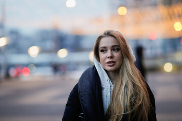 Fototapeta premium Caucasian girl woman in a long down coat in the city with a phone, the concept of safety and life in the city, communication