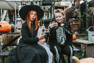 a boy in a skeleton costume and a girl in a witch costume with a dog in a ghost costume having fun on the porch of a house decorated to celebrate a Halloween party