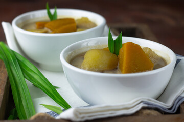 Kolak Ubi labu Kuning, Indonesian popular dessert made from pumpkin, sweet potato, coconut milk, and palm sugar. Served on ceramic bowl, garnished with pandan leaves. Close up view. 