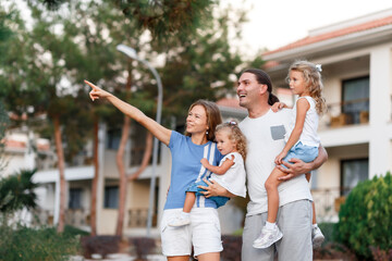 Beautiful family portrait, mom, father, small daughters, smiling outside next to their new house with sunset. Consept of new life in new house, life achivements.