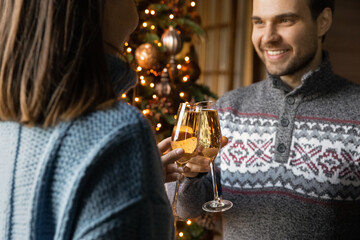 Close up of happy young Caucasian couple clink glasses greeting congratulating with New Year. Smiling millennial man and woman celebrate Christmas at home together. Holiday celebration concept.