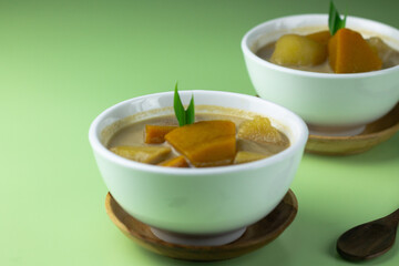 Kolak Ubi labu Kuning, Indonesian popular dessert made from pumpkin, sweet potato, coconut milk, and palm sugar. Served on ceramic bowl, garnished with pandan leaves. Close up view. 