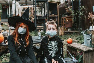 Obraz na płótnie Canvas a boy in a skeleton costume and a girl in a witch costume wearing a protective face mask at a Halloween party in a new reality due to the covid pandemic