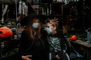 Fototapeta na wymiar a boy in a skeleton costume and a girl in a witch costume wearing a protective face mask at a Halloween party in a new reality due to the covid pandemic