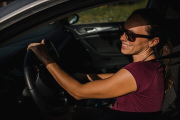 Naklejka na ściany i meble Woman in her car holding the steering wheel and smiling.