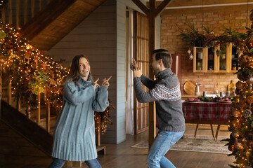 Overjoyed young Caucasian couple dance in decorated house celebrate New Year winter holidays together. Smiling happy man and woman have fun enjoy Christmas family celebration in own house.