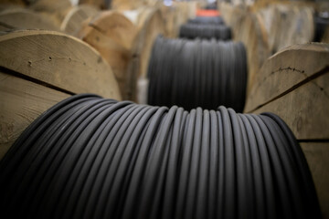 Vertical coils ndustrial wires. Many turns of main electrical cable is closeup. Roll of outdoor fiber optic signal shielded cables. Wooden Coils of powerful black telecommunications wire