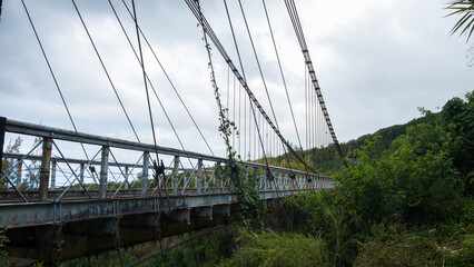 Old bridge with rusty cables suspended over the river