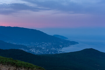 Fototapeta na wymiar Fantastically beautiful sunset over Yalta from AI-Petri mountain. Autumn mountain landscape. Blue and pink shades of clouds. A popular tourist destination. Cloudy evening post-sunset landscape.