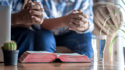 Close up the Bible on wooden desk with hands praying in background, church in home, Home church during quarantine coronavirus Covid-19, Religion concept.