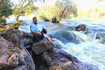 a young man sits on a stone on the banks of a stormy mountain river