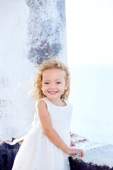 A beautiful little curly girl in white dress smiling outdoors